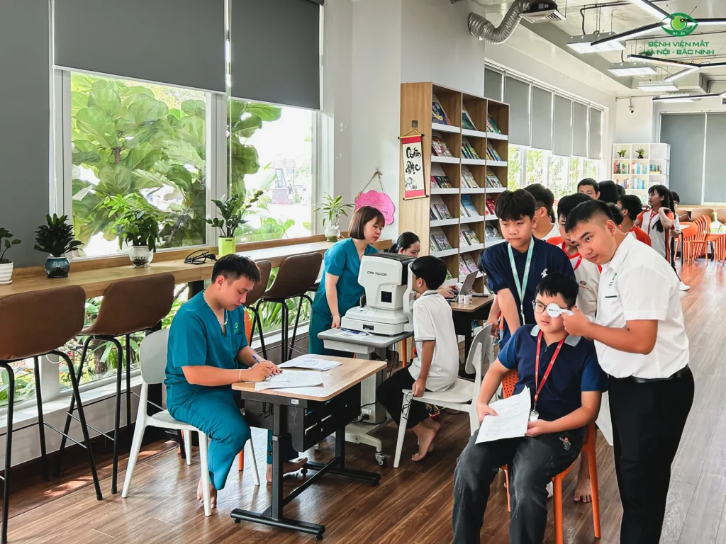 Học sinh được hỗ trợ che một mắt khi kiểm tra thị lực, cạnh khu vực kiểm tra bằng máy.