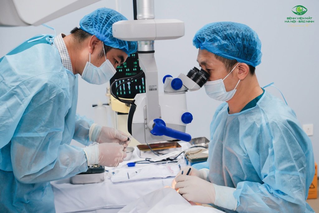 Nhân viên y tế phối hợp bên kính hiển vi phẫu thuật và bàn dụng cụ.