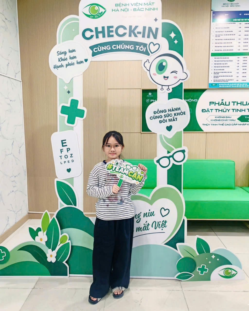 Khách nhỏ tuổi cầm bảng chụp ảnh tại góc check-in với khung trang trí màu xanh.