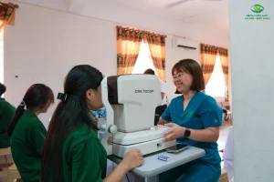 Nhân viên y tế hướng dẫn học sinh đo khúc xạ bằng thiết bị chuyên dụng.