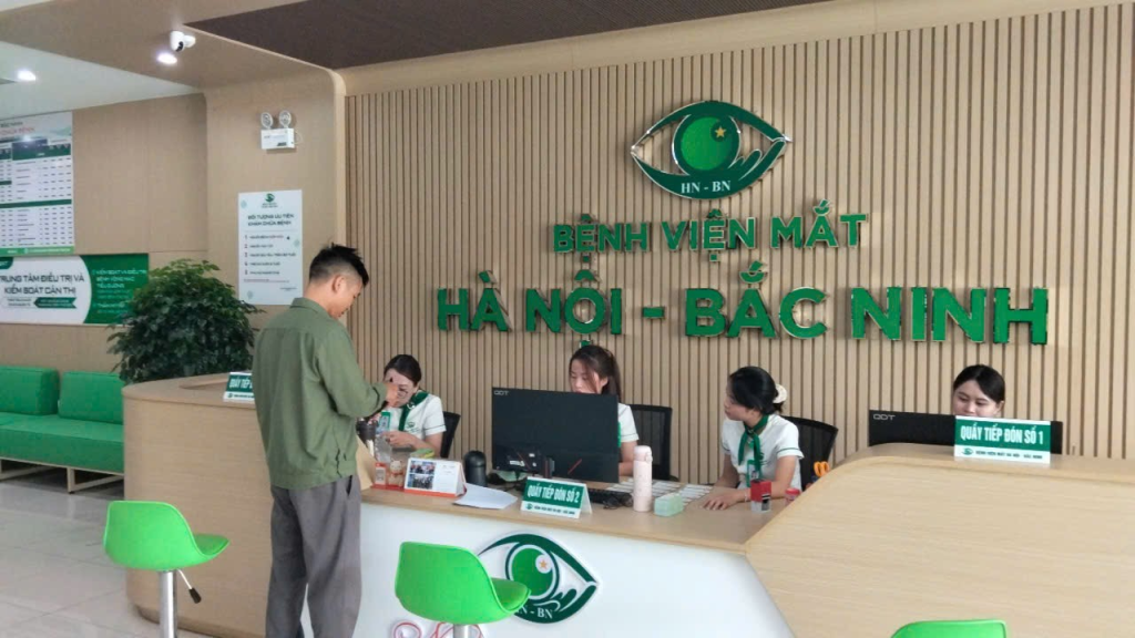 Một người đàn ông trao đổi với nhân viên tại quầy tiếp đón dưới biển tên Bệnh viện Mắt Hà Nội – Bắc Ninh.