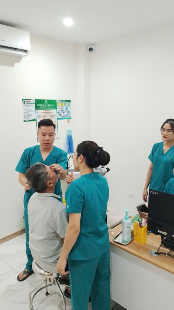 Nhân viên y tế đứng gần người bệnh lớn tuổi trong phòng khám, bàn thiết bị ở bên cạnh.