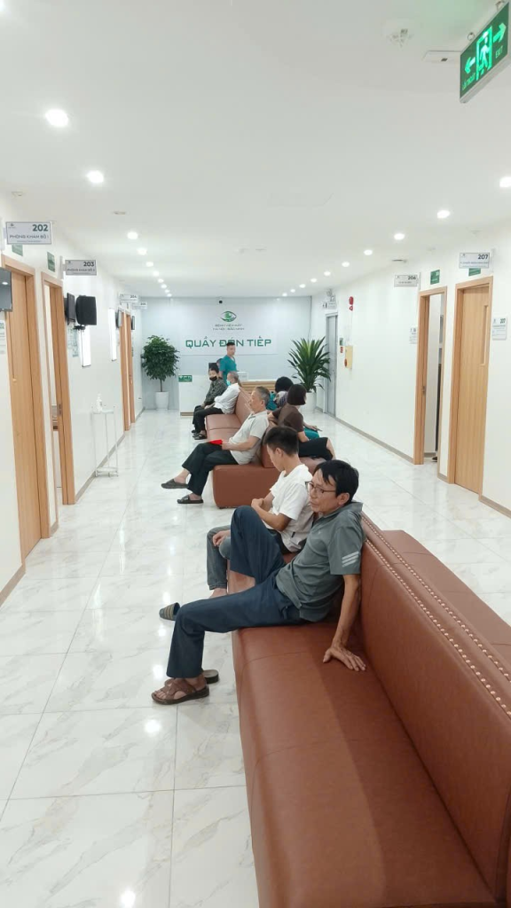 Người đến khám ngồi trên hàng ghế dọc hành lang các phòng chức năng tại bệnh viện mắt.